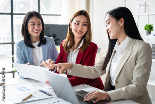 Three women are sitting at a table with laptops and papers
