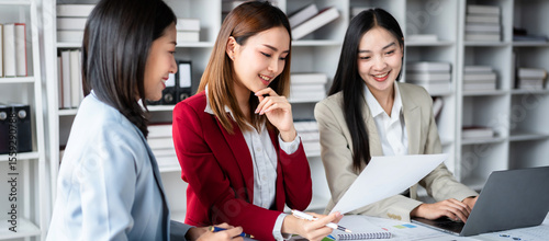 Three women are sitting at a desk with a white paper in front of them