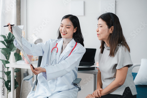 Asian Young Woman Doctor Explaining X-ray Results to Older Asian Woman Patient for Healthcare and Medical Consultation at Hospital Clinic