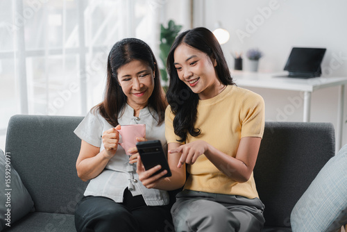 Asian Women Using Mobile Phone Together At Home Family Time Mother And Daughter Sharing Funny Content On Social Media Network And Drinking Beverage