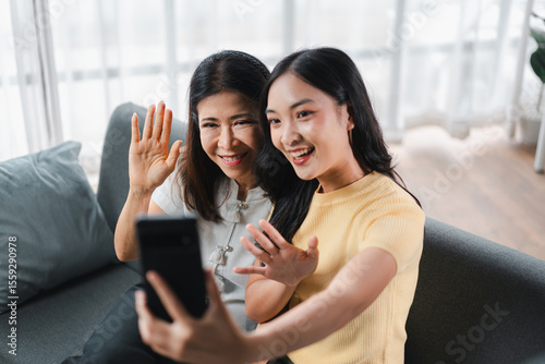 Asian Women Video Call Smiling and Waving Hands.  Happy Adult Daughter and Older Mother Connecting Online.  Family Communication Technology Concept for Mobile Lifestyle.