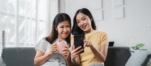 Asian Mother and Young Adult Daughter Using Smartphone on Sofa  Family Bonding Moment with Mobile Phone Technology and Happy Together  Social Media Sharing