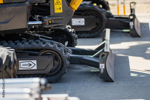 tracked construction vehicles with blade attachments on concrete surface, close up of heavy equipment with arrows and warning labels, industrial excavation and groundwork machinery display