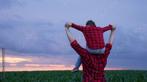 Caring father and cheerful son, exploring outdoors together, green maize plants, Holding hands and smiling faces, summer evening in farmland setting, Loving parent with child, wearing checkered shirts