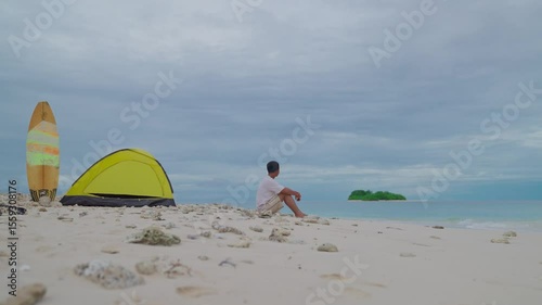 A man sits alone near a tent on the beach. A man enjoys his solitude on a tropical beach
