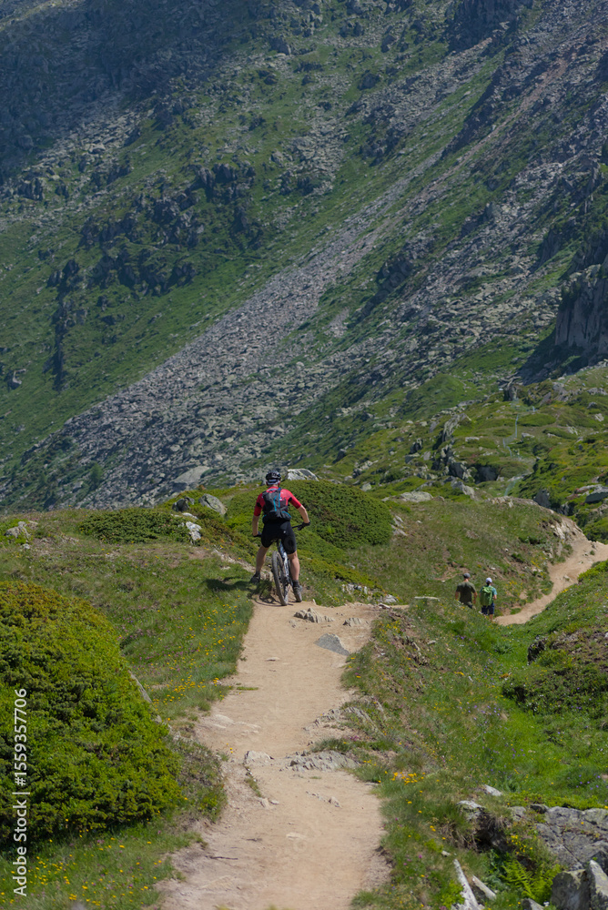 Fototapeta premium Experience mountain biking adventure! A cyclist conquers a rugged mountain trail under a bright sky, embodying the thrill of outdoor sports and exploration in a stunning alpine landscape.