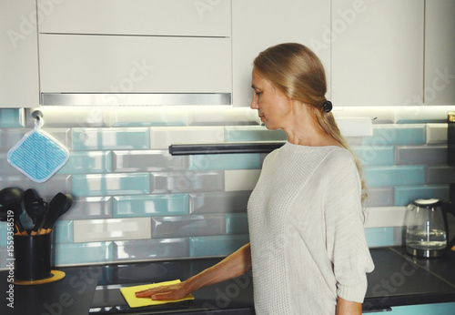 House cleaning, woman with microfiber rag wiping the surface cooker, kitchen countertop from dust
