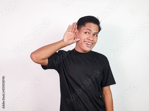 Casual portrait of a young man in a black shirt smiling while holding his hand to his ear, expressing attentiveness and curiosity in a friendly and approachable pose.