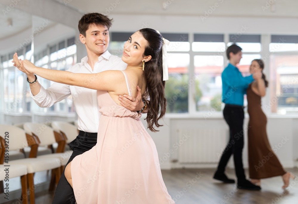 Fototapeta premium Girl and guy in festive clothes dancing slow ballroom dance during group lesson in a choreography studio