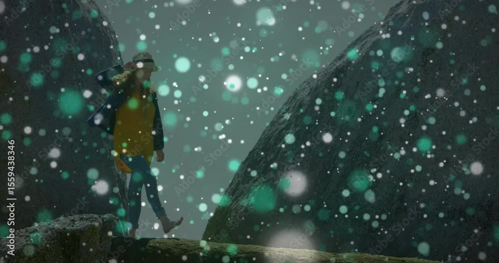 Travel blogger starting crossing ledge between boulders with falling snow adjusting hat for balance