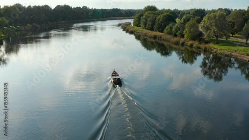An aerial shot captures a serene scene of a small wooden boat gliding smoothly across a tranquil river. 