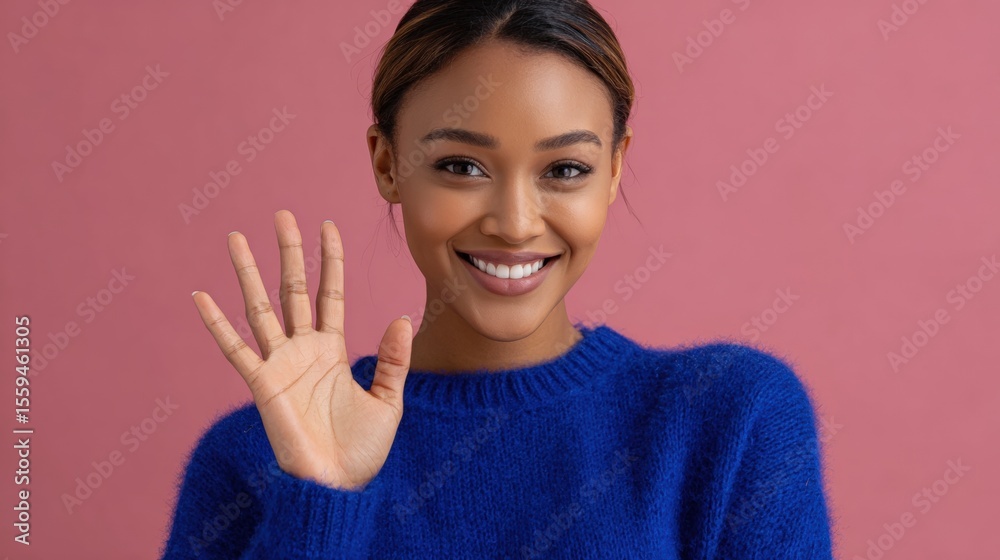 Smiling woman in a blue sweater waves against a pink background. Smiling woman in a blue sweater waves against a pink background.