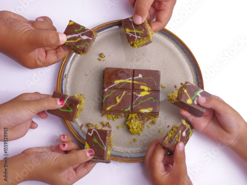 The children's hands take a piece of chocolate bar from the plate. Dubai chocolate bar with pistachio and milk filling and greentea isolated on white background, chocolate trend, delicious