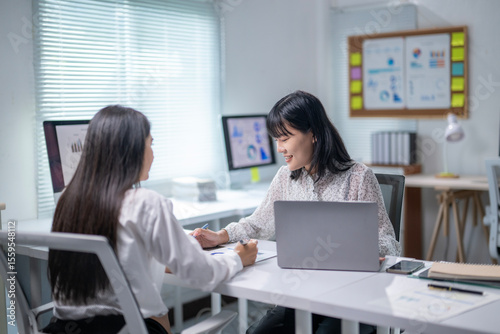 Two women are sitting at a desk, talking to each other