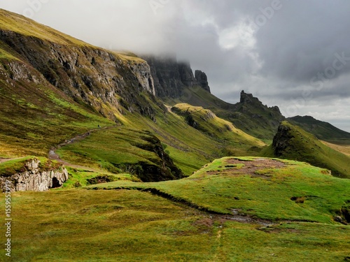 Dramatic landscape of Quiraing, Isle of Skye, Scotland. Rugged cliffs and lush green hills under moody skies. Ideal for nature, travel, and scenic photography.