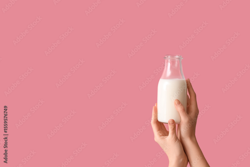Naklejka premium Hands holding bottle of milk on pink background