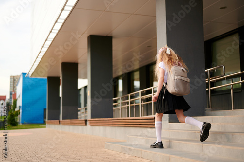 schoolgirl with backpack climbs steps of modern building. education concept with young student heading to school on sunny day. urban architecture enhances academic theme photo