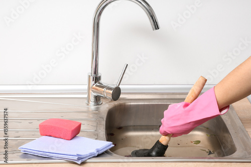 Photos Woman cleaning clogged sink with plunger in kitchen