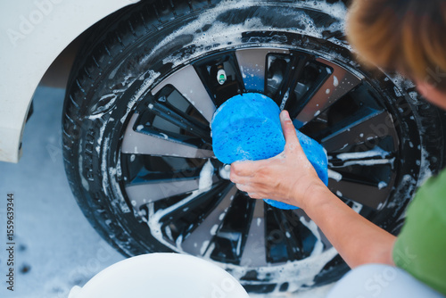 Obraz na plátně A middle-aged Asian man carefully washes his car using water and foam