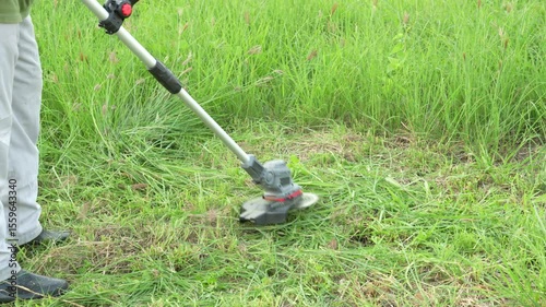 An Asian man is operating a cordless lawn mower to trim the grass. He appears focused and skilled, either maintaining his home garden or working professionally in outdoor landscaping.