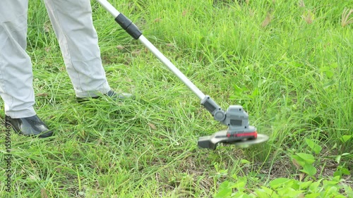 An Asian man is operating a cordless lawn mower to trim the grass. He appears focused and skilled, either maintaining his home garden or working professionally in outdoor landscaping.