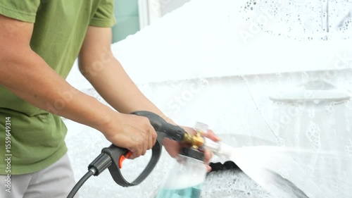 A middle-aged Asian man carefully washes his car using water and foam. Each step from high-pressure rinsing to scrubbing and drying ensures the vehicle is spotless, well-maintained, and presentable