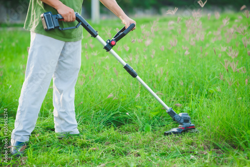 An Asian man is operating a cordless lawn mower to trim the grass. He appears focused and skilled, either maintaining his home garden or working professionally in outdoor landscaping.