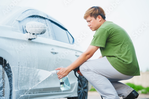 Schilderij op canvas A middle-aged Asian man carefully washes his car using water and foam