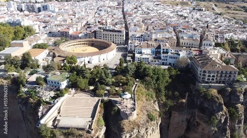 Aerial shot of circular Plaza de Toros bullring surrounded by white buildings and trees near steep cliffs, showcasing striking contrast between historic architecture and dramatic natural terrain.