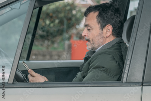 middle-aged man checking his cell phone in the car