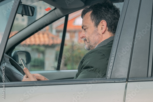 middle-aged man checking his cell phone in the car
