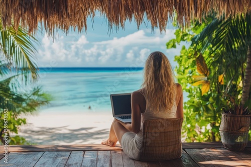 Fototapeta Naklejka Na Ścianę i Meble -  Woman enjoying remote work under palm shadow on wooden terrace, beach vacation background