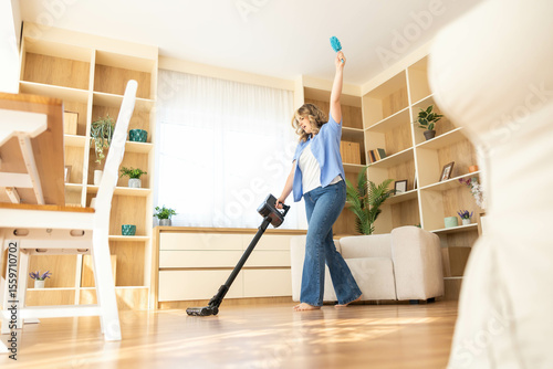 A woman joyously celebrates while vacuuming her home, demonstrating a positive and upbeat approach to household chores.