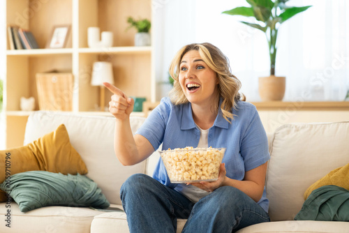 The woman laughs joyfully, pointing at the screen while watching a movie, highlighting her enjoyment of the cinematic experience.