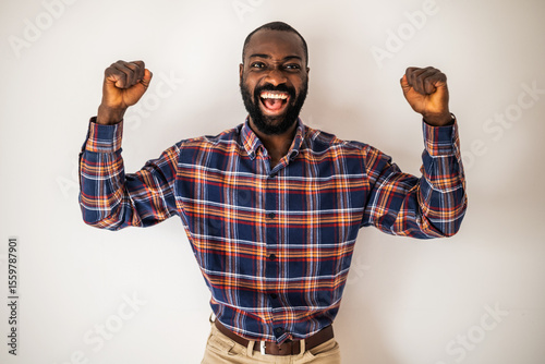 Cheerful black man in cozy shirt shirt standing in front of wall and smiling. He is raising his arms in euphoria.