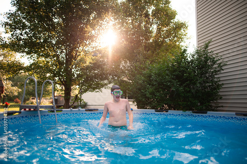 Teen splashes in backyard pool on sunny summer day