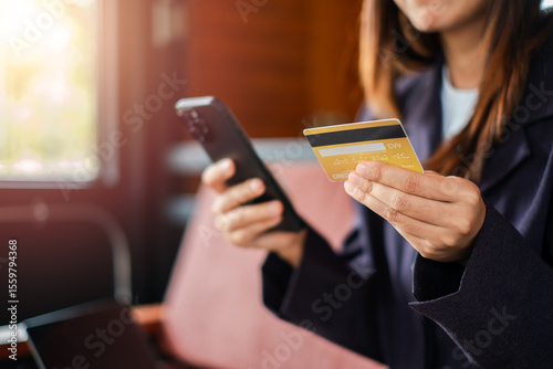Woman using smartphone and credit card for online shopping in a cafe, highlighting digital payment and e-commerce.