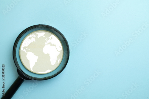 Global research concept. A magnifying glass focusing on a world map symbol on a blue background. Represents international business, globalization, searching for global trends.,copy space for text.