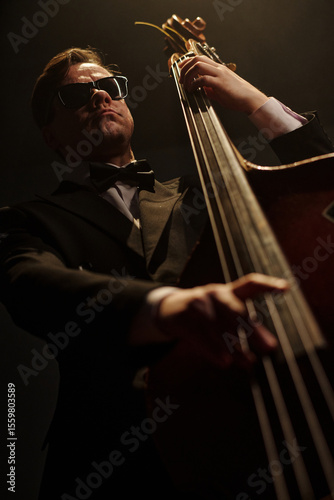 Canvas Print Caucasian middle aged man wearing sunglasses playing double bass on stage, holdi
