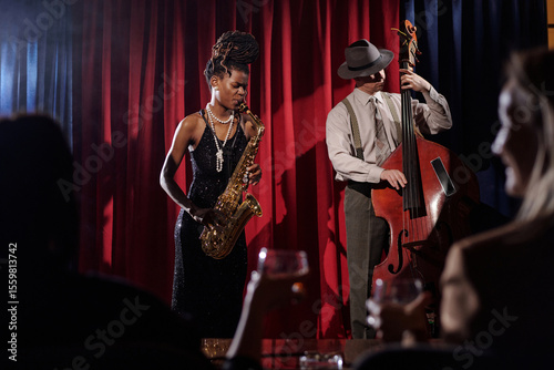 Photography Black young adult woman playing saxophone and Caucasian middle aged man playing