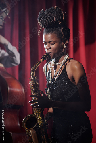 Canvas Print Young adult Black woman playing saxophone on stage, eyes closed, wearing jewelry