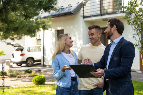 Real estate agent discussing property details with couple using clipboard in front of house