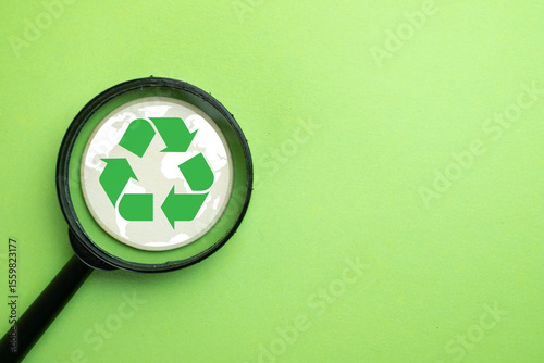 Recycling and environmental protection concept. A magnifying glass focuses on a green recycle symbol over a world map. Represents sustainability, waste management, going green, and eco-friendly.