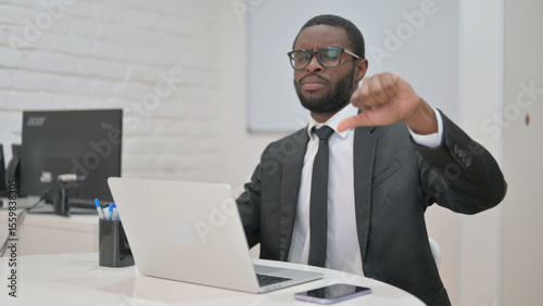 Disapproving African American businessman showing a thumbs-down gesture from his office desk