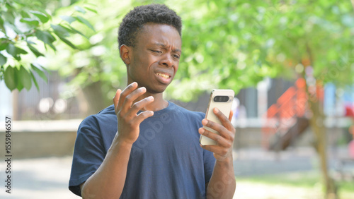 Upset Casual African Man Reacting to Phone Content Outdoors