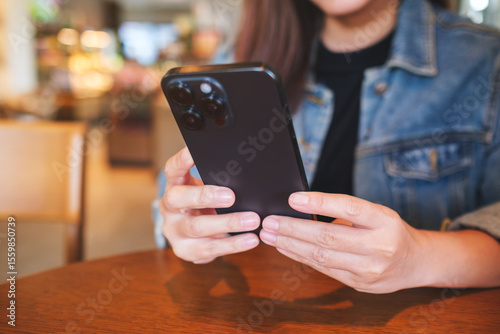 Closeup image of a woman holding and using mobile phone in cafe