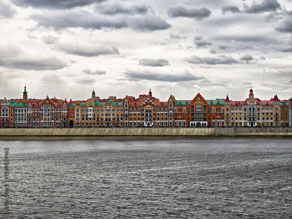 Fototapeta premium Colorful historic buildings line the Bruges embankment by the river in Yoshkar-Ola under a cloudy sky