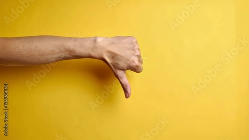 Hand gesturing thumbs down on a plain yellow background suggesting negativity, rejection, dislike or disapproval