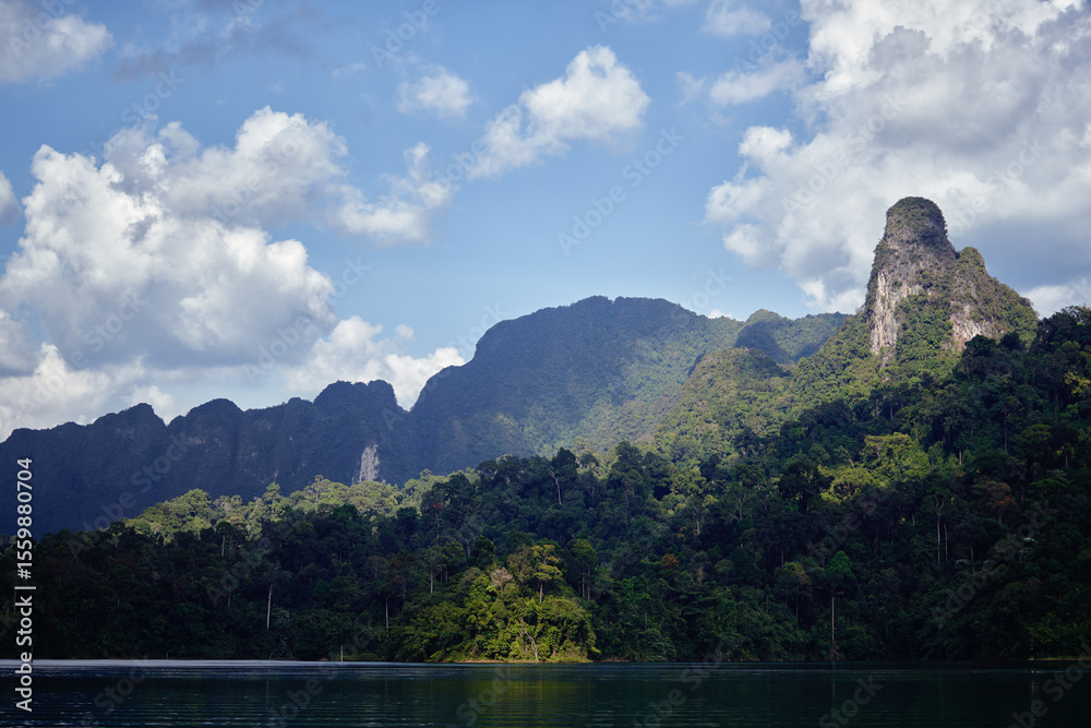 Naklejka premium Scenic View of Verdant Jungle With Towering Mountain Peaks and Blue Sky