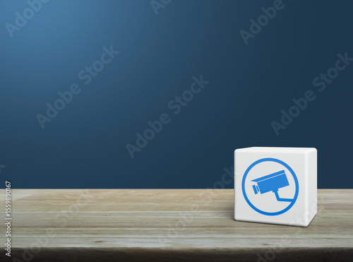 Cctv camera flat icon on white block cube on wooden table over light blue wall, Technology security and safety online concept